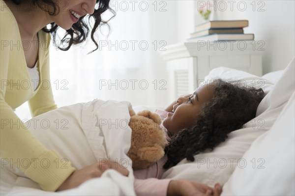 Mother tucking daughter into bed