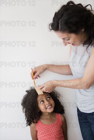 Mother measuring height of daughter against wall