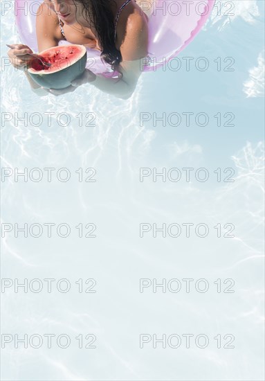 Caucasian woman eating watermelon in swimming pool