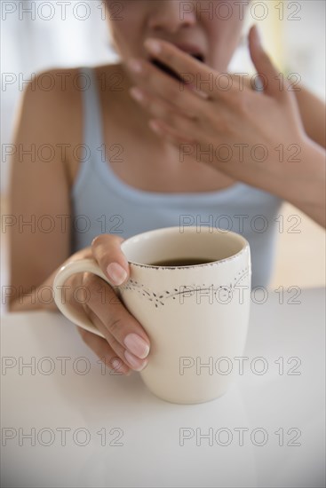 Yawning Hispanic woman drinking coffee