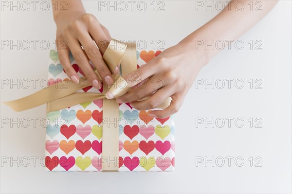 Hispanic woman tying ribbon on gift