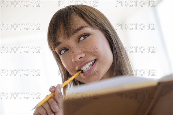 Mixed race woman chewing pencil and reading