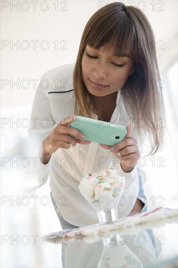 Mixed race woman photographing dessert