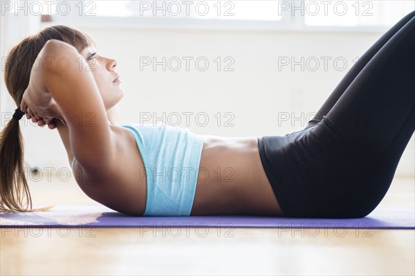 Mixed race woman doing sit-ups on yoga mat