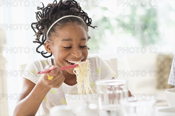 Black girl eating noodles at table