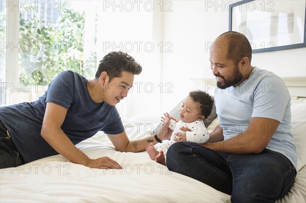 Gay fathers playing with baby son on bed