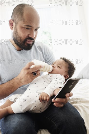 Father bottle feeding baby son and using cell phone