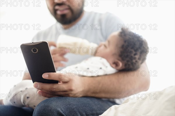 Father bottle feeding baby son and using cell phone