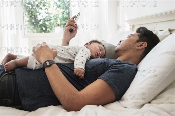 Father using cell phone with sleeping baby son