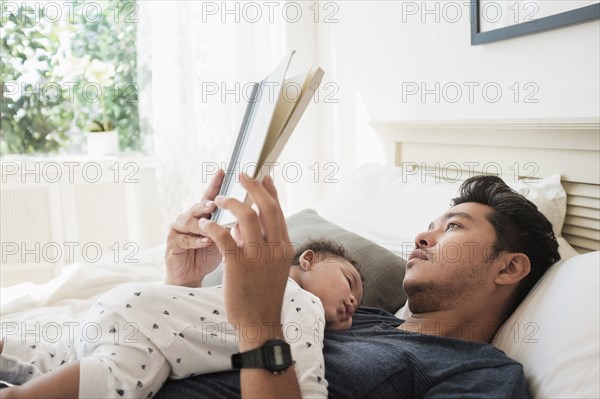 Father reading with sleeping baby son