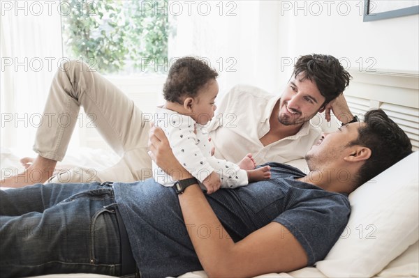 Gay fathers playing with baby son on bed