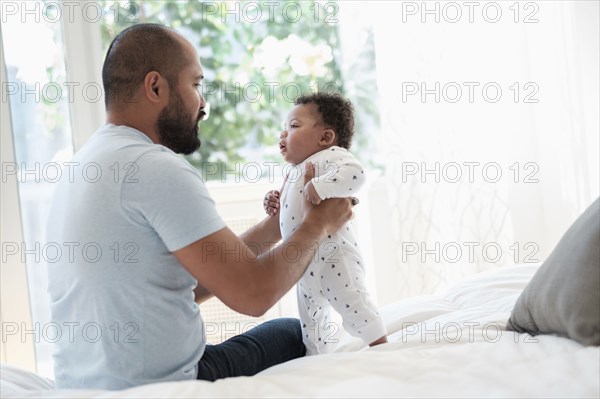 Father playing with baby son on bed