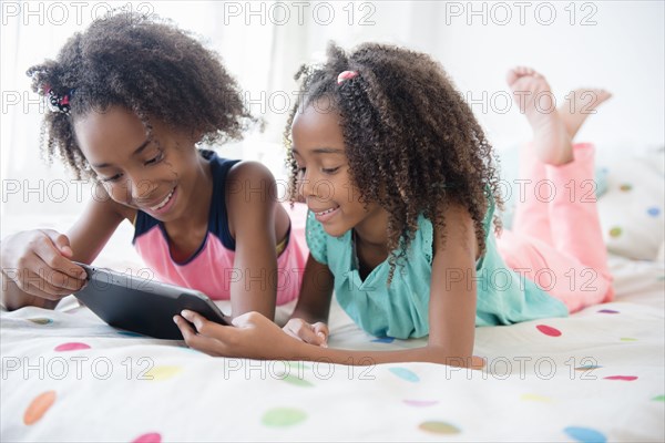 Mixed race sisters using digital tablet on bed