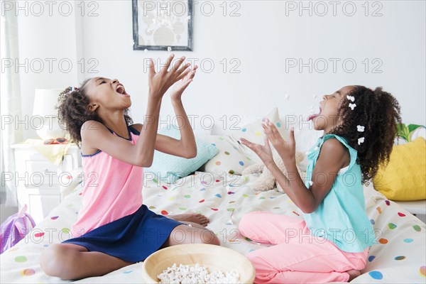 Mixed race sisters eating popcorn on bed