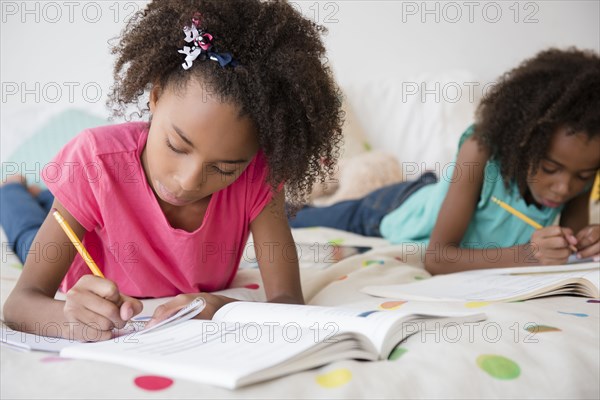 Mixed race sisters doing homework on bed
