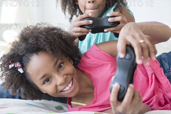 Mixed race sisters playing video games on bed