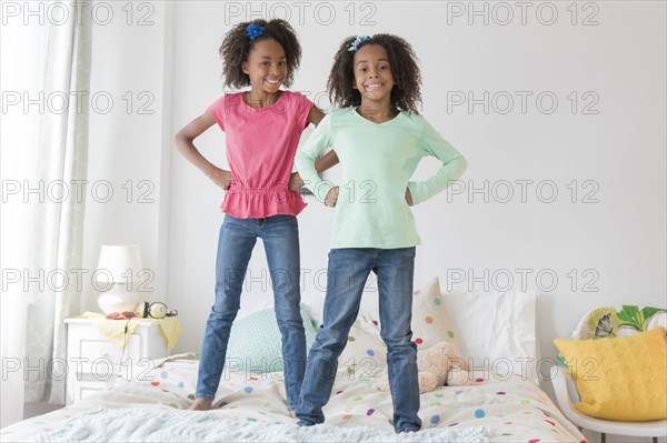 Mixed race sisters standing on bed