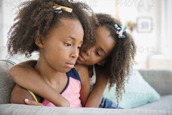 Mixed race sisters hugging on sofa