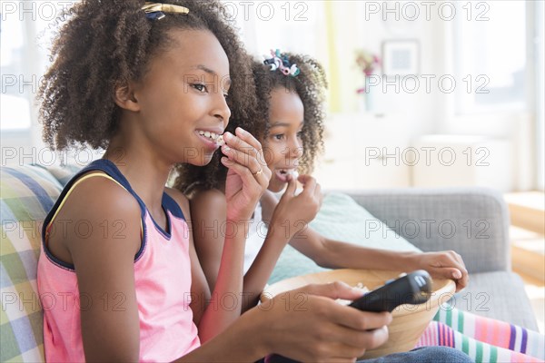 Mixed race sisters watching television on sofa