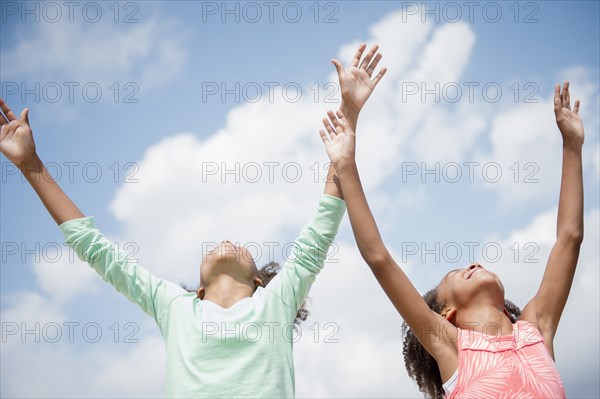 Mixed race sisters cheering in blue sky