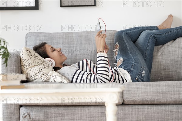 Mixed race woman listening to headphones on sofa