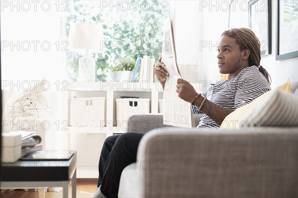 Mixed race man reading newspaper on sofa