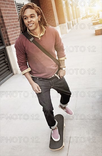 Mixed race man riding skateboard on sidewalk