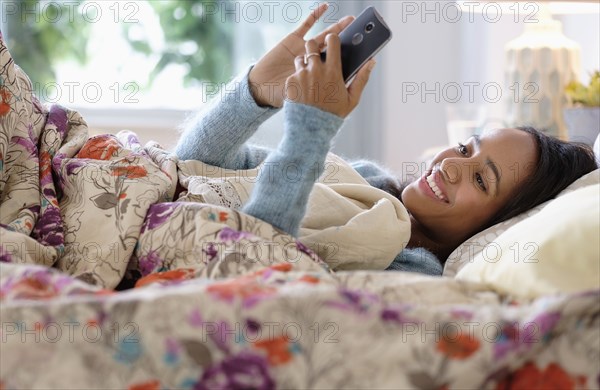 Mixed race woman using cell phone in bed