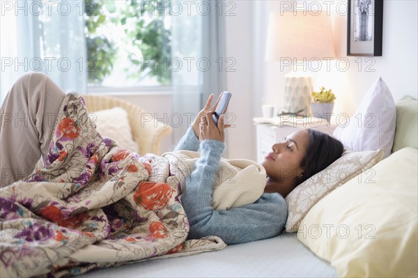 Mixed race woman using cell phone in bed