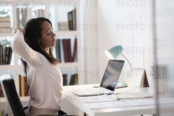 Mixed race businesswoman stretching at desk