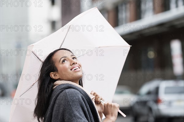 Mixed race woman carrying umbrella outdoors