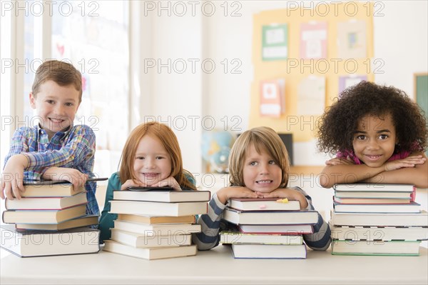 Students resting on stacks of books in classroom