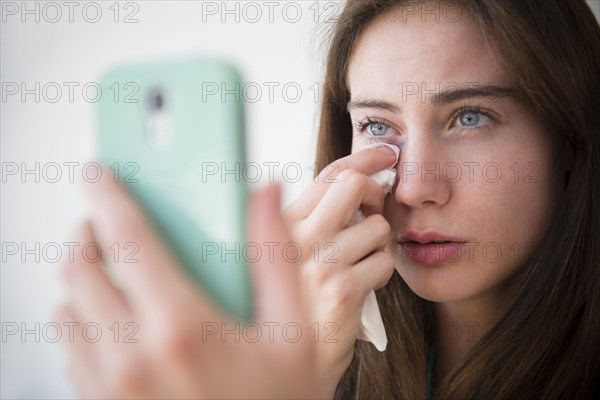 Native American woman with cell phone wiping away tears