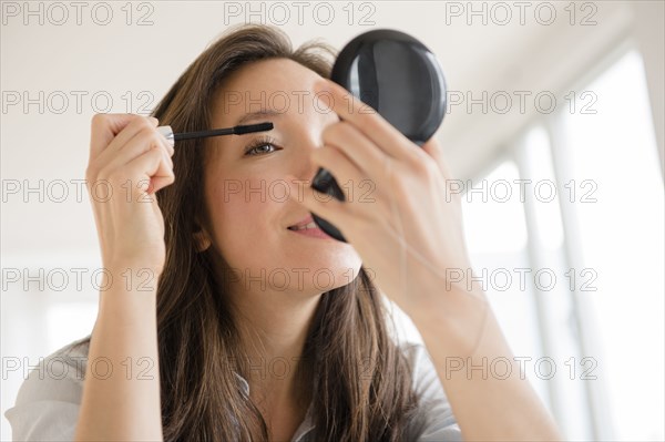 Mixed race woman applying makeup in compact mirror