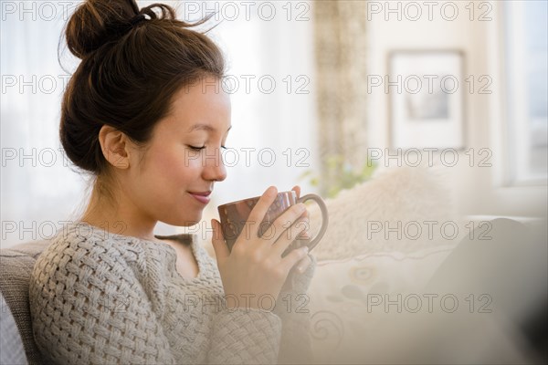 Mixed race woman drinking coffee on sofa