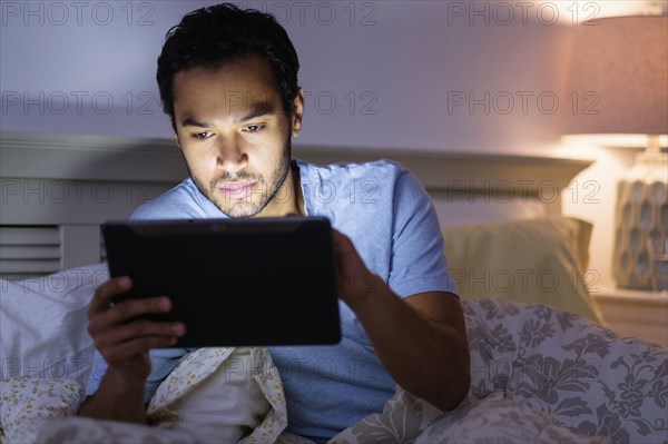 Hispanic man using digital tablet in bed