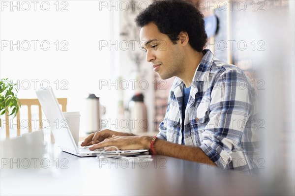 Mixed race man using laptop in coffee shop