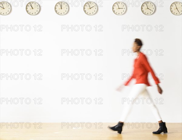 Mixed race businesswoman walking under clocks