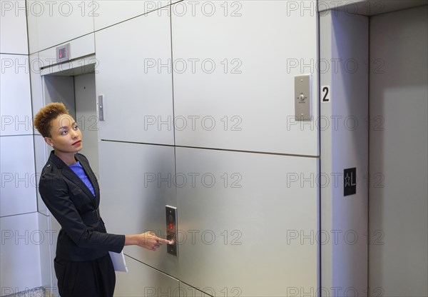 Mixed race businesswoman pressing elevator button