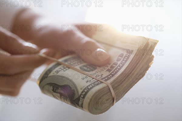 Hispanic woman holding rubber band around wad of cash