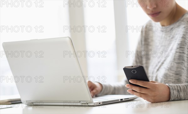 Hispanic woman using cell phone and laptop