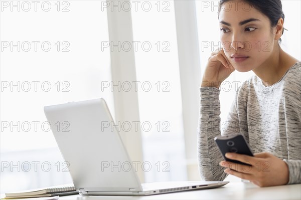 Hispanic woman using cell phone and laptop