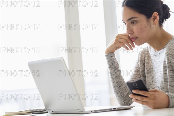 Hispanic woman using cell phone and laptop