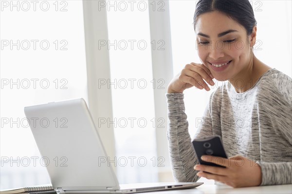 Hispanic woman using cell phone and laptop