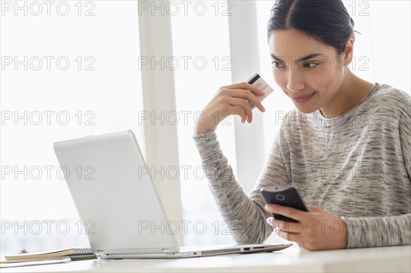 Hispanic woman shopping on cell phone and laptop