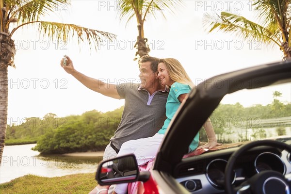 Caucasian couple taking selfie on convertible