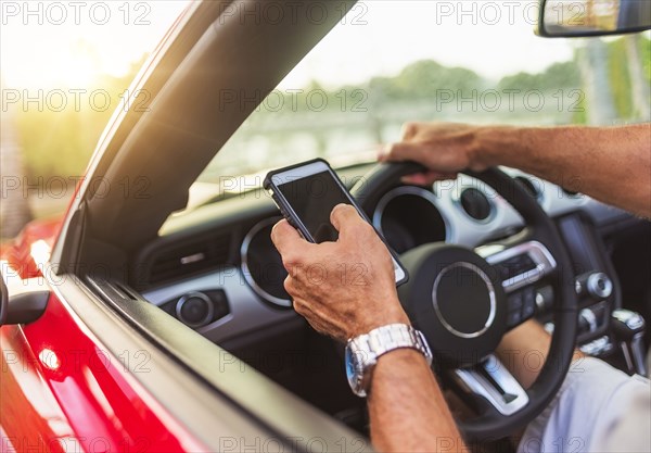 Caucasian man using cell phone and driving convertible