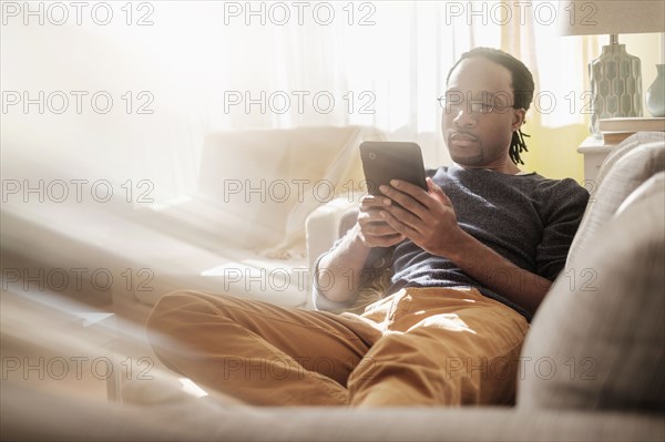 Black man using digital tablet on sofa