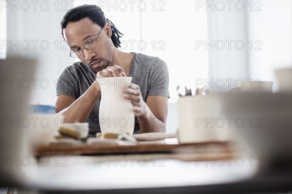 Black artist shaping ceramic vase in studio