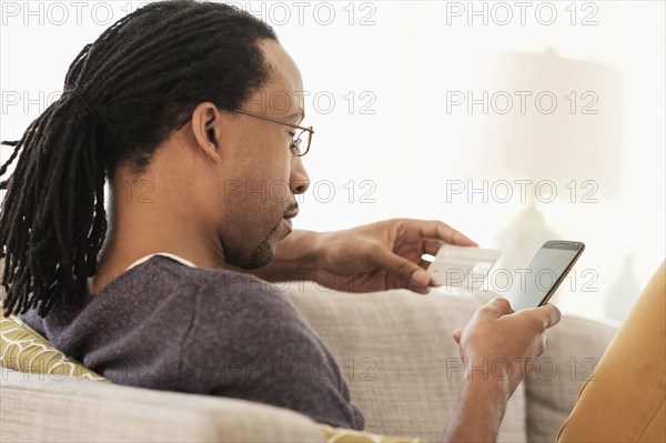 Black man shopping with cell phone on sofa